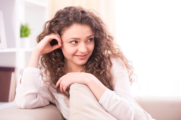 De jonge glimlachende vrouw zit thuis op een laag.