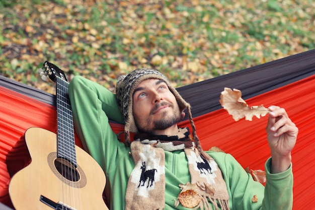 De jonge hipstermens met gitaar ontspant in een hangmat in het de herfstbos. val stemming concept.