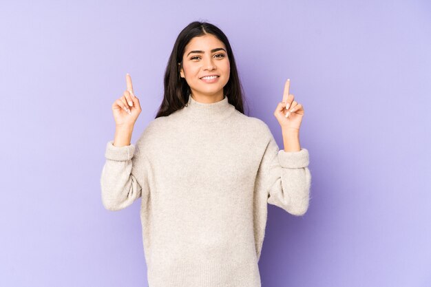 De jonge Indische vrouw die op paars wordt geïsoleerd, geeft aan met beide wijsvingers omhoog het tonen van een lege ruimte.