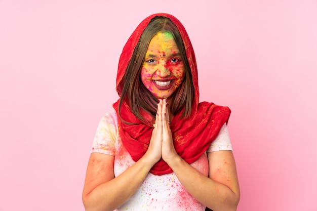 De jonge Indische vrouw met kleurrijk holipoeder op haar gezicht op roze muur houdt palm samen. Persoon vraagt om iets