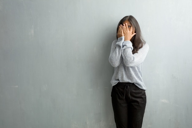 De jonge Indische vrouw tegen een grungemuur voelt zich ongerust gemaakt en doen schrikken, kijkend en behandelend FA