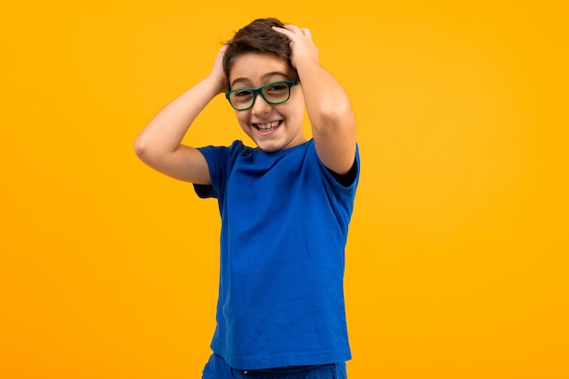 De jonge jongen in een blauw T-shirt met glazen houdt zijn hoofd op geel met exemplaarruimte