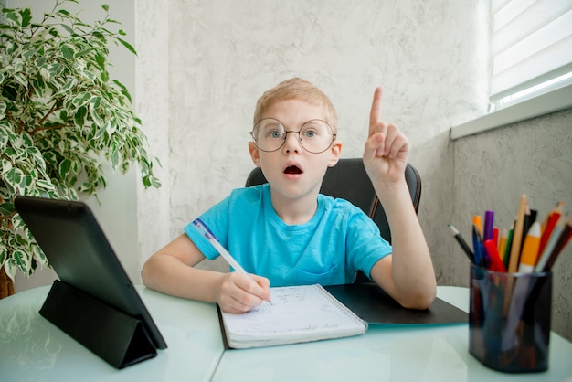 De jonge jongen leert thuis door tablet. Afstandsonderwijs in quarantaine.