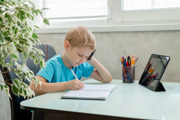 De jonge jongen leert thuis door tablet. Afstandsonderwijs in quarantaine.