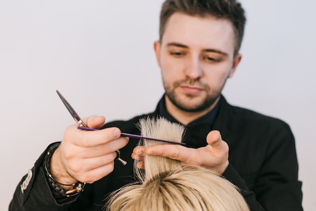 De jonge kapper houdt en snijdt een bundel van wit haar van vrouw in de schoonheidsstudio.