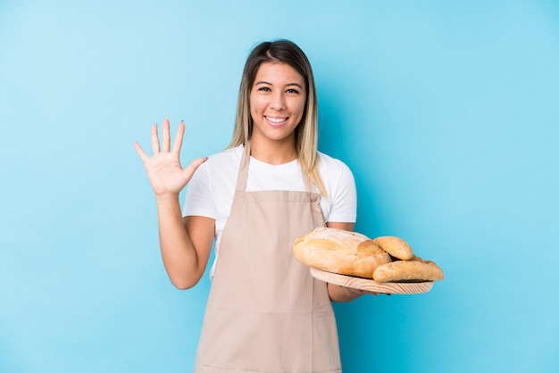 De jonge kaukasische bakkersvrouw isoleerde het glimlachen vrolijk tonend nummer vijf met vingers.