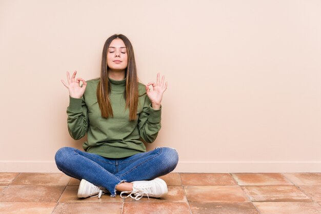 De jonge Kaukasische geïsoleerde vrouwenzitting op de vloer ontspant na harde werkdag, voert zij yoga uit.