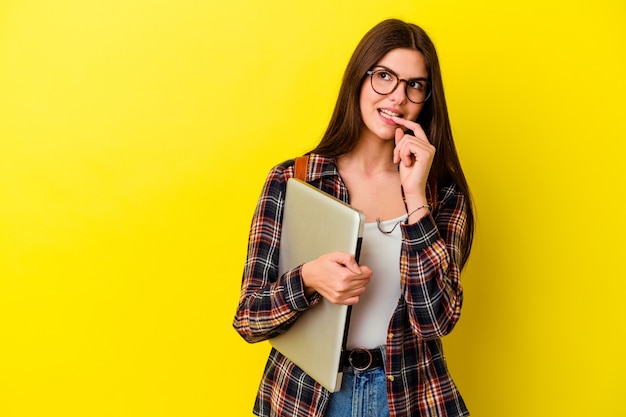 De jonge kaukasische studentenvrouw die laptop houden die op roze muur wordt geïsoleerd ontspant denkend over iets dat een exemplaarruimte bekijkt.