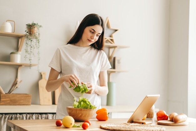 De jonge kaukasische tabletcomputer van het vrouwengebruik in de keuken