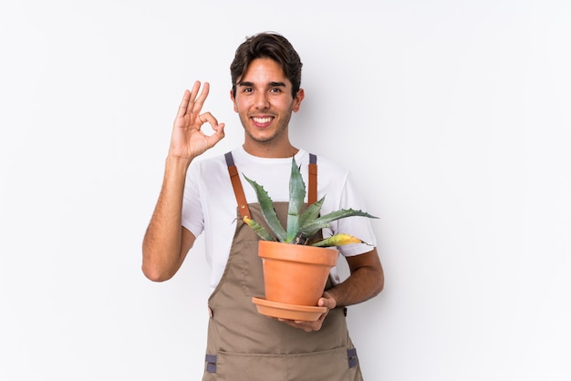 De jonge kaukasische tuinmanmens die een installatie houden isoleerde vrolijk en zeker tonend ok gebaar.