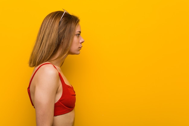 De jonge kaukasische vrouw die bikini en zonnebril draagt die links, zijwaarts staart stelt.