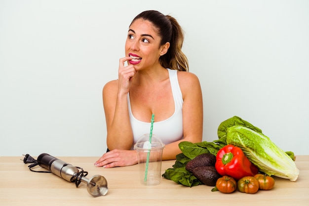 De jonge kaukasische vrouw die een gezonde smoothie met groenten voorbereidt ontspant het denken over iets dat een exemplaarruimte bekijkt.