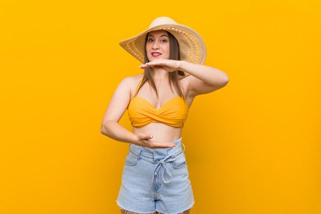 De jonge Kaukasische vrouw die een strohoed, de zomer draagt kijkt holding iets met beide handen, productpresentatie.