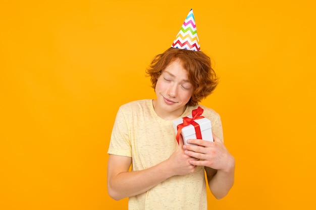 De jonge Kaukasische vrouw houdt een witte doos met gift en heeft heel wat emoties die op sinaasappel worden geïsoleerd