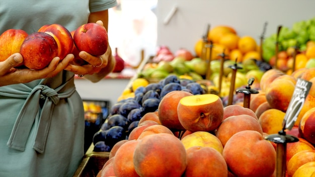 Foto de jonge kaukasische vrouw kiest een rijpe nectarines bij supermarkt. close-up van vrouwelijke handen neemt perziken uit de plank.