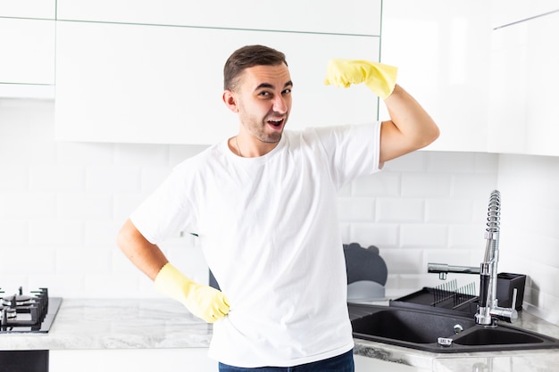 De jonge knappe man toont macht in handschoenen na het schoonmaken van de keuken thuis