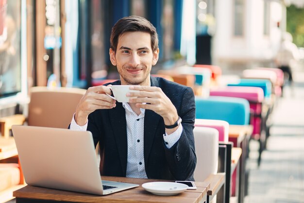 De jonge knappe mens geniet van koffie die aan laptop werkt