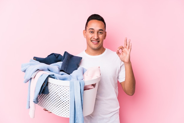 De jonge Latijnse mens die vuile kleren opnemen isoleerde vrolijk en zeker tonend ok gebaar.