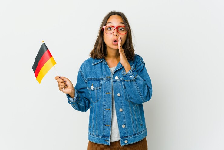 Foto de jonge latijnse vrouw die een duitse vlag houdt die op witte achtergrond wordt geïsoleerd, zegt een geheim heet remmend nieuws en kijkt opzij
