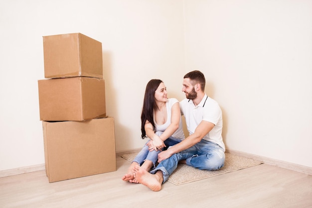 De jonge man en vrouw zitten op de grond naast dozen en kijken elkaar aan