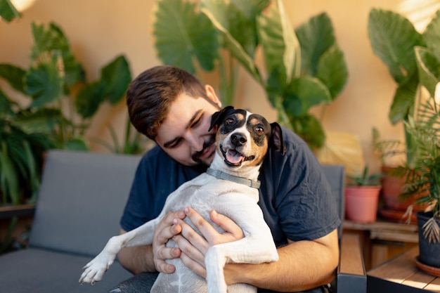 Foto de jonge man glimlacht en houdt zijn hond vast terwijl hij met zijn poten speelt. de hond kijkt naar de camera.