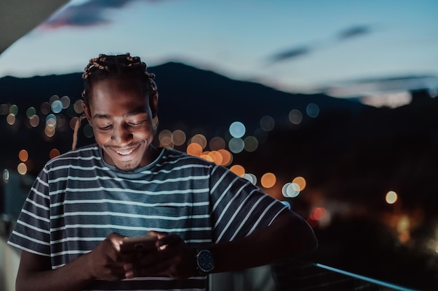 Foto de jonge man op een stedelijke stadsstraat 's nachts sms't op een smartphone met bokeh en neon stadslichten op de achtergrond. foto van hoge kwaliteit. foto van hoge kwaliteit