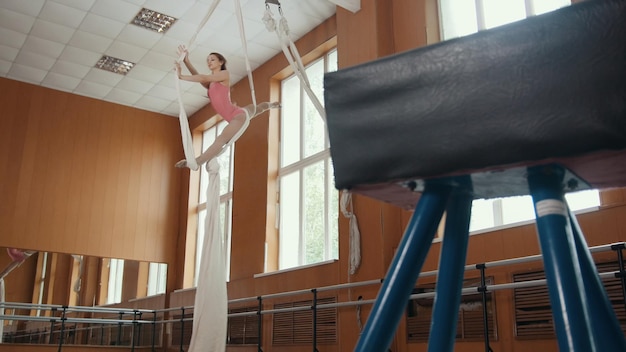 De jonge meisjesacrobaat toont flexibiliteit op gymnastiekhoepel, telefotoschot