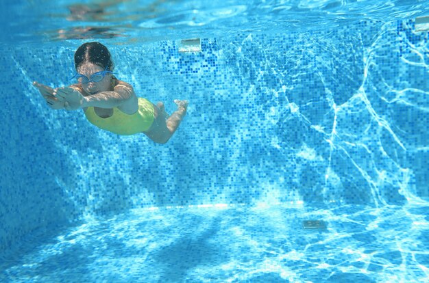 De jonge meisjeszwemmer die onder water in pool zwemmen en heeft pret, tiener onderwater duiken, familievakantie, sport en fitness concept