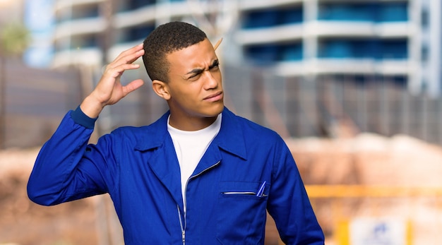 De jonge mens die van de afro amerikaanse arbeider twijfels heeft terwijl het krassen van hoofd in een bouwwerf