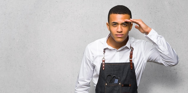 De jonge mens die van de afro Amerikaanse kapper ver weg met hand kijken om iets op geweven muur te kijken