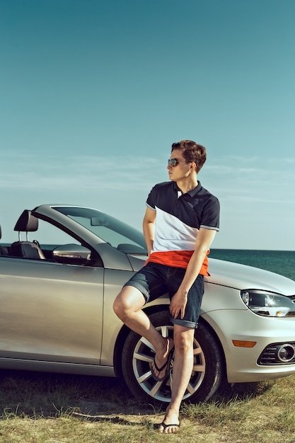 De jonge mens drijft een auto op het strand