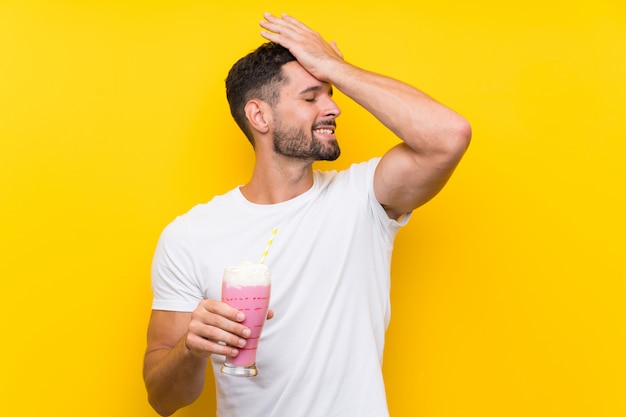 De jonge mens met aardbeimilkshake over geïsoleerde gele muur heeft iets gerealiseerd en de oplossing voornemens