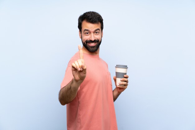 De jonge mens met baard die haalt koffie over geïsoleerde blauwe muur houden weg en opheffend een vinger