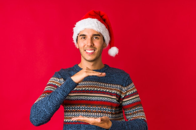 De jonge mens op Kerstmisdag knipoogt een oog en houdt een ok gebaar met hand.