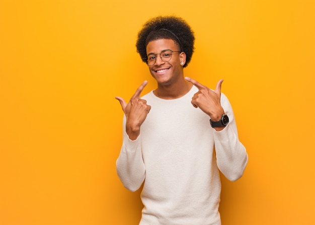 De jonge mens over een oranje muur glimlacht, wijzend mond