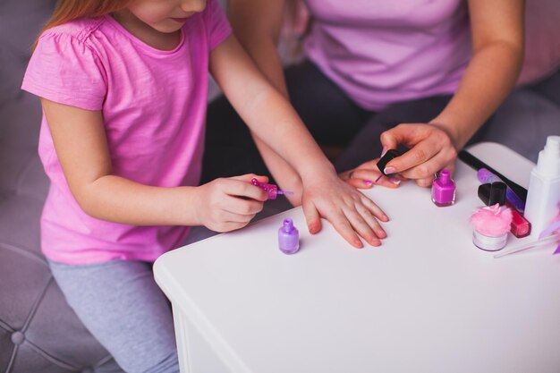 De jonge moeder en dochtertje doen manicure Moeder en dochter gekleed in roze T-shirts zitten in de kamer