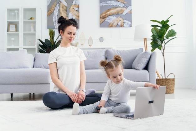 De jonge moeder en haar aanbiddelijke dochter gebruiken laptop terwijl het liggen op de vloer.