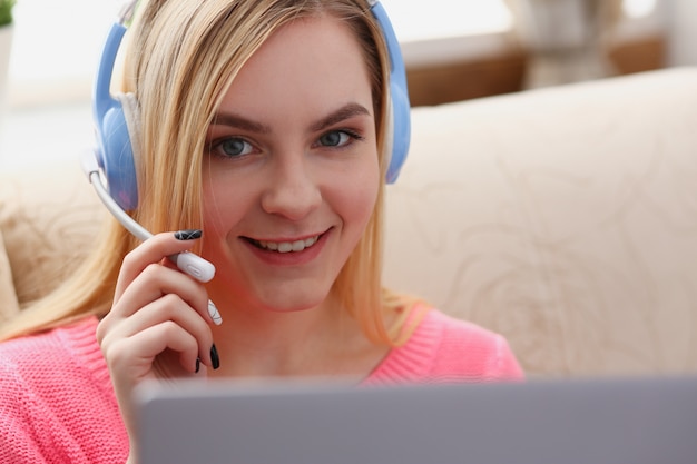 Foto de jonge mooie blonde vrouw zit op de bank in laptop van de woonkamergreep in wapens luister aan muziek