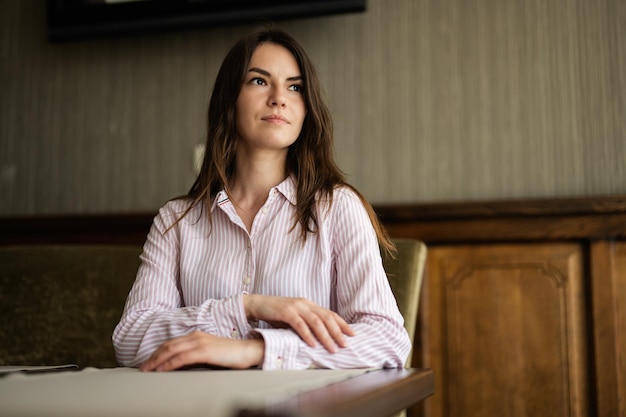 De jonge mooie donkerbruine vrouw zit binnen in het café-restaurant van de coffeeshop