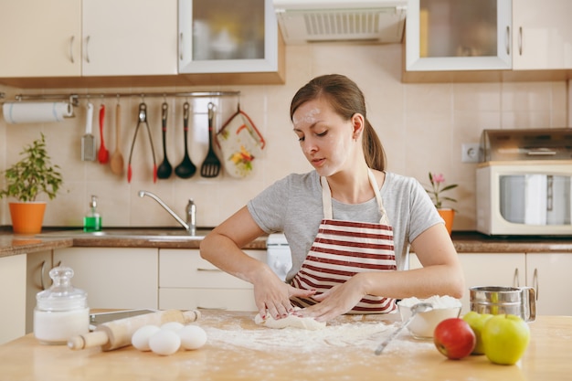 De jonge mooie gelukkige vrouw zit aan een tafel met bloem, kneed deeg en gaat een taart in de keuken bereiden. thuis koken. eten koken.