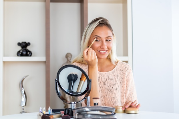 De jonge mooie vrouw die haar doet maakt omhoog dichtbij spiegel