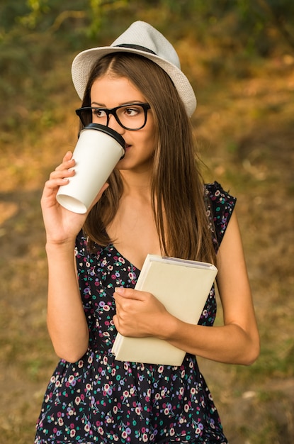 De jonge mooie vrouw in hoed en glazen drinkt koffie.