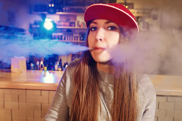 De jonge mooie vrouw in rood glb rookt een elektronische sigaret bij de vape-winkel