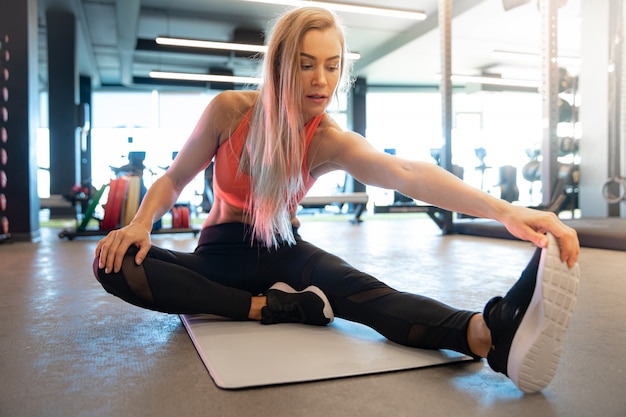 De jonge mooie vrouw rekt zich in de gymnastiek vóór oefening uit