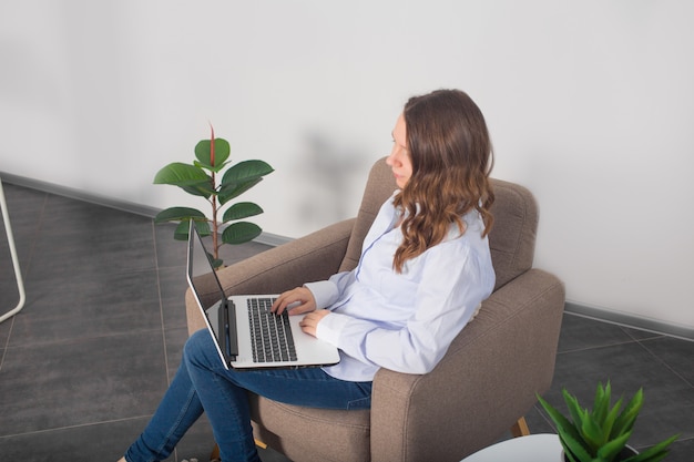 De jonge mooie vrouw werkt met computer van huis