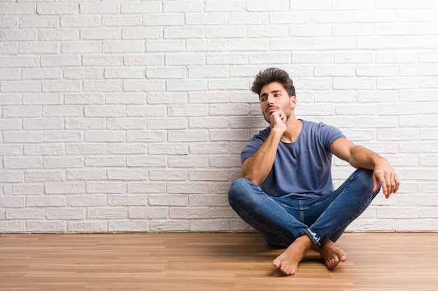 De jonge natuurlijke mens zit op een houten en vloer die omhoog denken, verward over een idee kijken