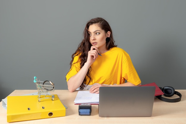 De jonge online winkelmanager zit aan een bureau op kantoor en werkt met een laptop en documenten