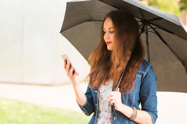 De jonge paraplu van de vrouwenholding en in openlucht het spreken op celtelefoon op regenachtige dag