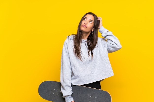De jonge schaatservrouw over geïsoleerde gele muur die twijfels hebben en verwart gezichtsuitdrukking