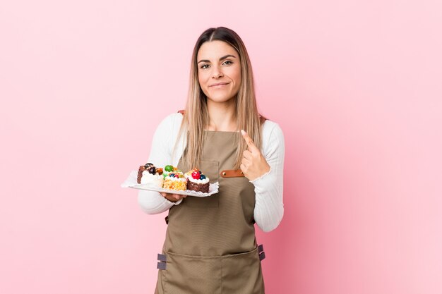 De jonge snoepjes die van de bakkersvrouw holding met vinger op u richten alsof uitnodigend dichter komen.